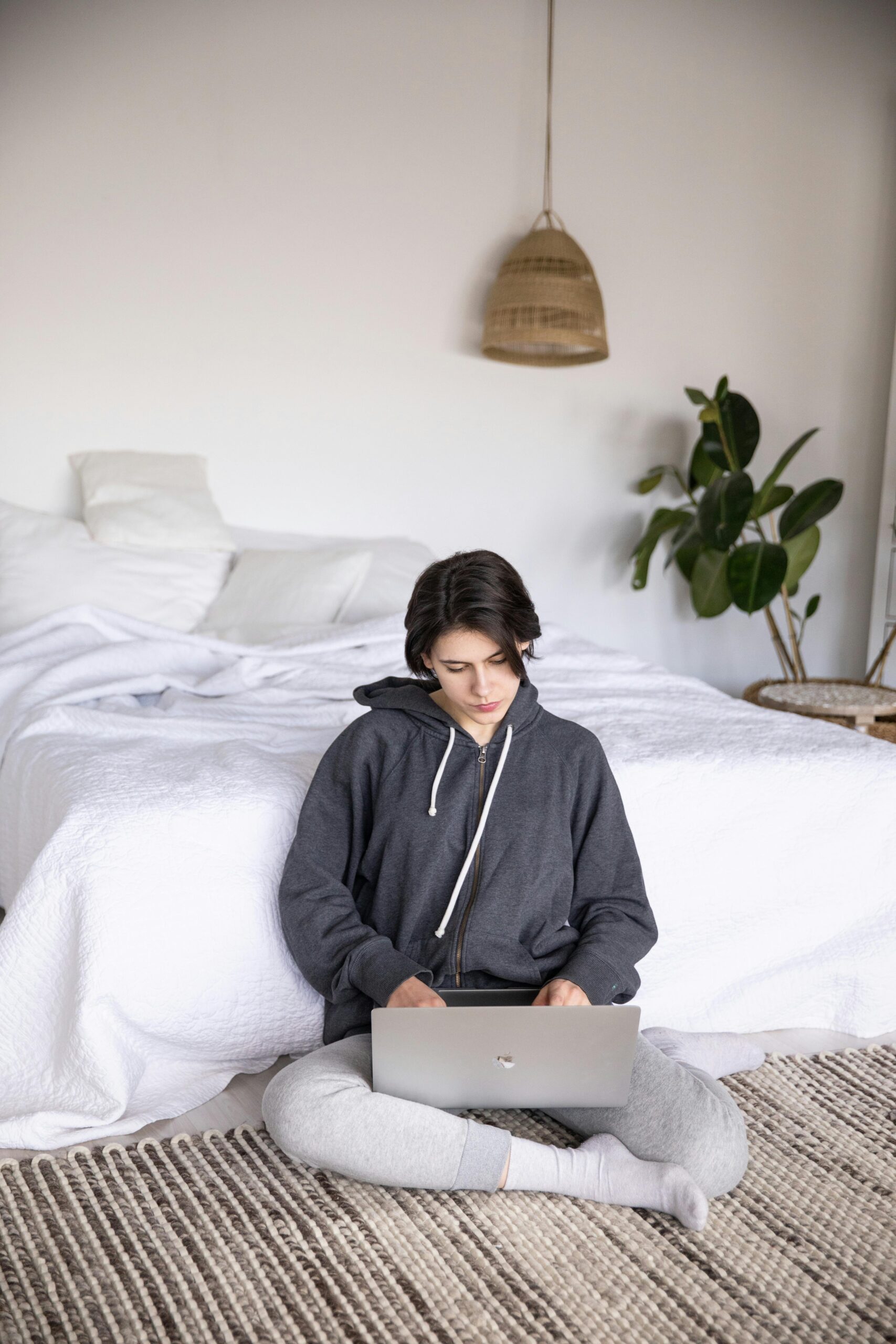 Woman working on a laptop in a cozy, modern bedroom with stylish decor.